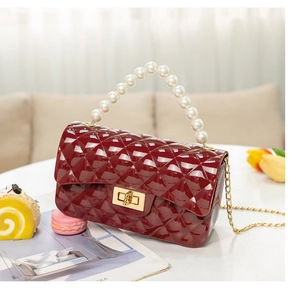 Close-up of wine red quilted handbag with pearl handle and golden chain on white table