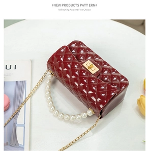 Detail of burgundy jelly bag with quilted texture, pearl handle, and gold chain strap
