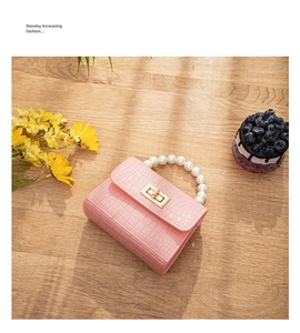 Pink croc-effect mini jelly bag with pearl handle on table next to dessert