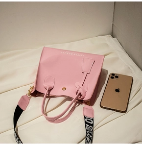 Détail du sac à main en cuir verni rose avec bandoulière lettrée et un smartphone