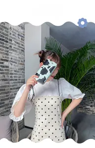 Cow print long wallet in blue with wristlet strap shown in model's hand outdoors