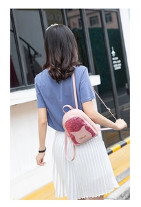 Rear street view of model wearing a pink cat-themed sequin mini backpack with ears