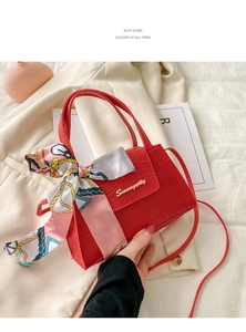 Detail of red croc-embossed handbag featuring silk scarf handle and metal logo