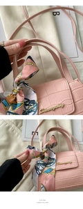 Detailed view of pink crocodile pattern handbag with silk scarf and gold logo buckle