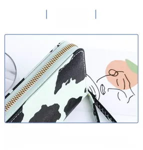 Close-up of cow print pattern on long synthetic leather wallet with gold zipper detail