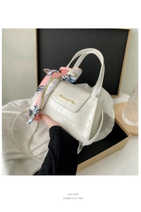 Detail of white crocodile texture handbag with pink silk scarf and gold metal logo plate