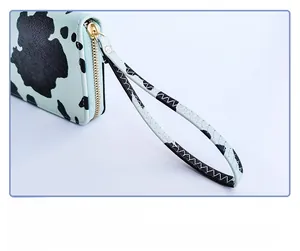 Detail of cow pattern long wallet featuring light blue trim and golden zipper with wrist strap