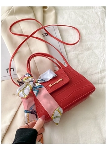 Detail of red crocodile texture handbag featuring a decorative silk scarf on the handle