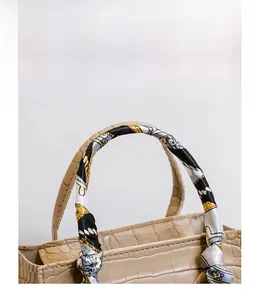 Detail eines Griffs der Krokoprägung-Handtasche mit dekorativem Seidenschal umwickelt