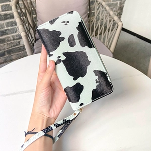 Long cow print clutch wallet with wristlet strap and zipper for women on marble table