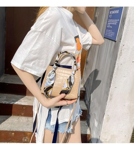 Beige Handtasche mit Krokodilprägung und dekorativem Seidenschal am Griff im Freien