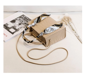 Detail der beigen Handtasche mit Krokodilprägung und dekorativem gebundenem Seidenschal