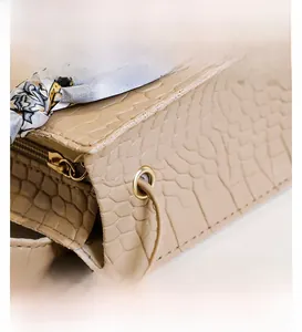 Details einer beigen Handtasche mit Krokostruktur, goldener Hardware und Seidenschal