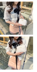 Close-up of white quilted camera bag with golden metal logo and wide woven shoulder strap