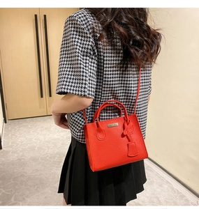 Red pebbled leather crossbody bag shown on model with stylish black pleated skirt