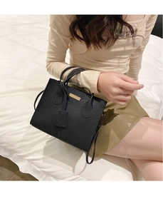 Detail of black litchi texture handbag with gold plaque and dual handles held by model