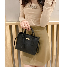 Detail of black litchi textured leather handbag with gold hardware and side tag