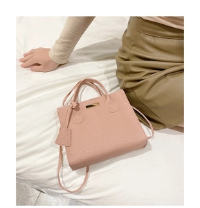 Detail of pink lychee texture faux leather handbag with golden metal trim on the bed