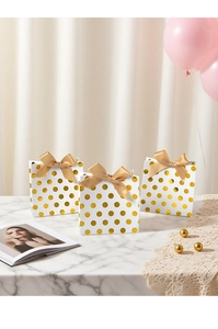 Detail of small white gift bags with gold foil dots and elegant golden silk bow accents