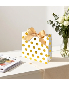 Elegant gift bag with gold polka dots and a large satin bow displayed on a wooden table
