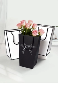 Minimalist black trapezoid gift bag with white bow print and pink roses inside