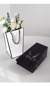 Minimalist trapezoid gift bag in white with black trim and a bow pattern gift box