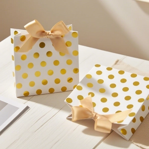 White gift bags with gold foil dots and champagne satin bows on a light wood surface