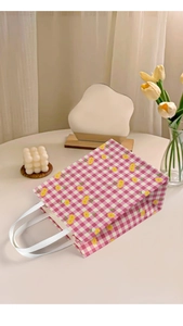 Detail of pink floral checkered gift bag with white ribbon handles on a soft desk setup
