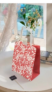 Close-up of vintage embossed gift bag with red scroll pattern and white ribbon bow