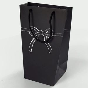 Minimalist black paper gift bag featuring a white hand-drawn bow and woven rope handles