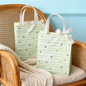 Elegant green striped gift bags with white silk bows on a cozy wicker chair