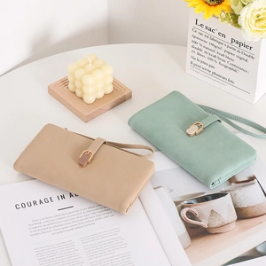 Long PU leather wallets in apricot and mint green with wrist straps on a white table