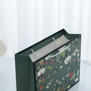 Detailed close-up of dark green floral paper gift bag with white rope handles