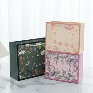 Detail of floral printed paper gift bags with braided handles on marble surface