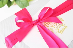 Macro view of bright neon pink polyester satin ribbon tied in a bow on white gift box