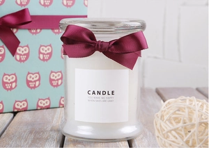 Close-up of white scented candle in glass jar with burgundy grosgrain ribbon bow