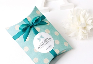 Detalle de caja de regalo de lunares verde azulado con cinta de seda y etiqueta de gala