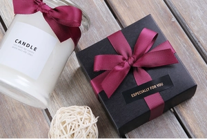 Gift box with burgundy grosgrain ribbon bow and scented candle on wooden surface