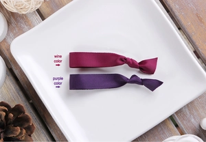 Close-up of wine red and purple ribbed grosgrain knot hair ties on a white ceramic plate