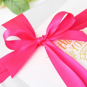 Magenta satin ribbon tied in an elegant bow on a white textured gift box