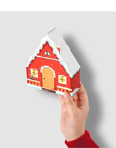 Detail of hand holding a red house-shaped gift box with snowy white roof and gold dots