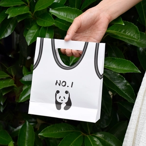 White paper gift bag with cartoon panda and jersey design held against green leaves