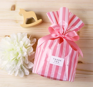 Pink and white striped gift bag with silk ribbon and Thank You sticker on wooden background