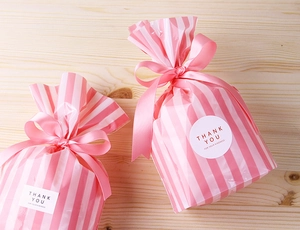 Detailed view of pink and white striped gift bags with ribbon bows and thank you stickers