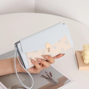 Détail du portefeuille long bifold avec imprimé cœur, dragonne et fermoir trèfle en métal