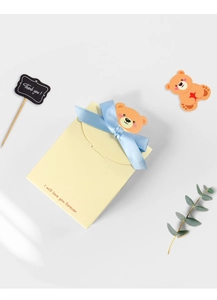 Flat lay of yellow folding gift envelope with blue silk bow and cute bear ornament