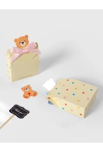 Close-up of yellow bear gift box with pink ribbon and heart pattern details
