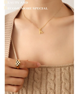 Gros plan sur le collier lettre H doré et la bague coeur avec émail en damier