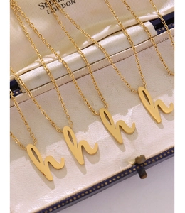 Gros plan de quatre pendentifs lettre 'h' sur chaînes dorées dans un coffret à bijoux