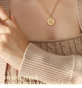 Detail of layered gold portrait coin necklace and chain ring on knit sweater background
